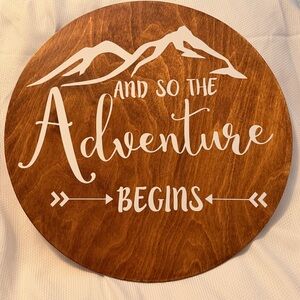 Round Wooden Wall Sign "And So The Adventure Begins" - White on Warm Brown
